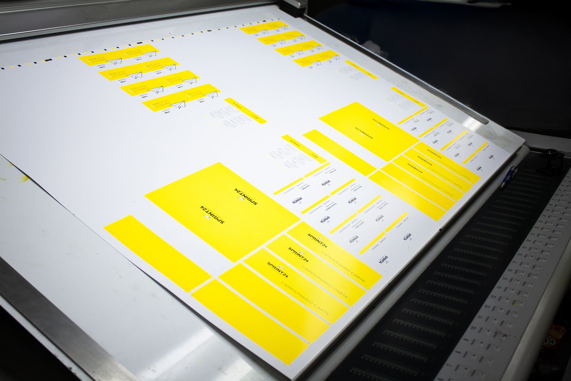 A large-format press sheet with yellow color calibration blocks sits on a professional digital printing machine at Sprint24. This image represents the high-quality offset and digital printing process at the heart of Sprint24's online typography services. Our state-of-the-art machinery ensures precise color accuracy and consistent results for all printed products.