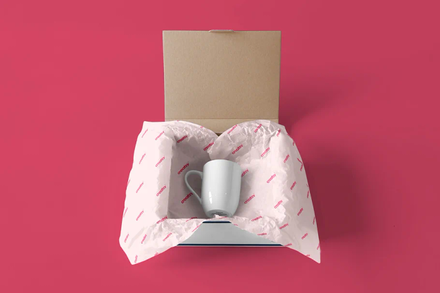 This custom pink packaging paper with repeating pattern elegantly protects a white mug inside a kraft cardboard box. The personalized wrapping demonstrates how custom packaging preserves products while creating a premium unboxing experience. Ideal for showcasing items in customized wrapping paper that enhances your brand presentation.