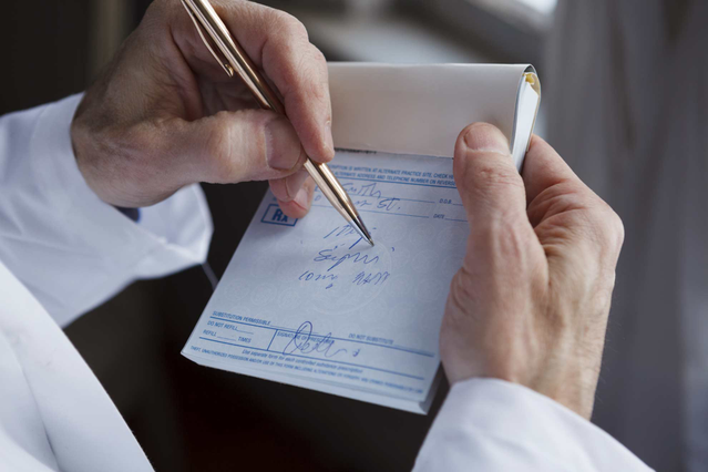 A doctor in a white coat writing on a personalized medical prescription pad held in hand, using a gold pen. Sprint24 prints custom medical prescription pads with letterhead for doctors, GPs, veterinarians and clinics — ideal for creating professional, branded prescription notepads that distinguish your practice and include your contact details.