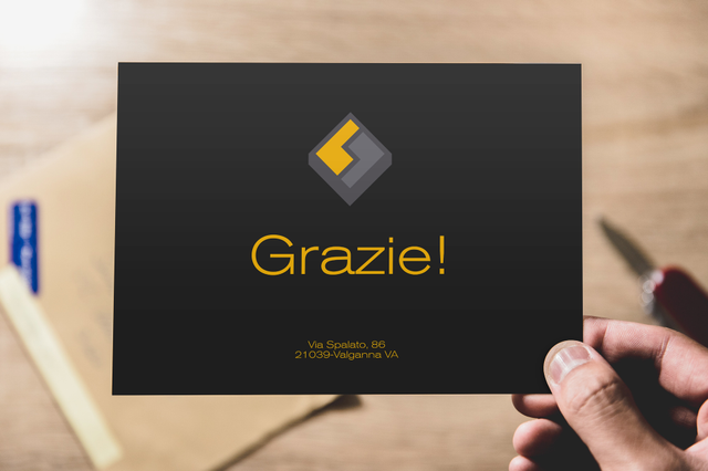 Hand holding black Grazie thank you card with gold diamond logo on wood desk. Custom Fedrigoni print Sprint24.