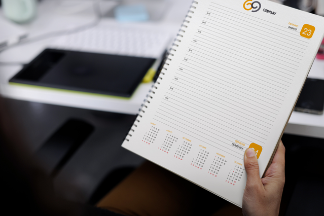 Hand holding open spiral daily agenda with orange G9 logo, date stamp and monthly mini-calendar. Sprint24.