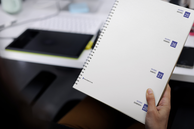 Hand holding open spiral weekly agenda two-page weekly spread with. Hand holding open spiral weekly agenda with two-page spread and blue date stamps. 128 pages Fedrigoni Sprint24.
