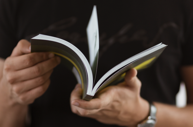Hands holding open a professionally printed perfect-bound paperback book. Sprint24.