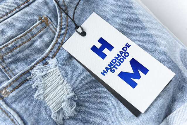 A custom clothing care label tag with hot foil branding attached to a blue denim jeans fabric. Sprint24 prints personalised hot foil stamped clothing tags in multiple metallic finishes including silver, gold and rose gold — ideal for fashion brands, boutiques and clothing designers seeking elegant branded labels that convey premium quality.