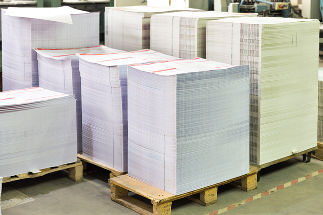 Wooden pallets stacked with large quantities of printed machine sheets in a print production warehouse. Sprint24 prints small machine sheets in bulk for typographers and print professionals who handle their own cutting and finishing — ideal for high-volume offset jobs, batched flyers and cost-efficient large-run print campaigns.