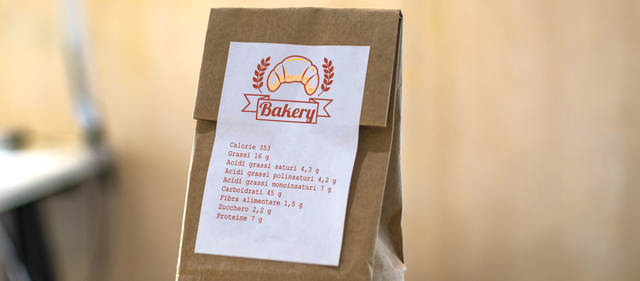 White adhesive paper label with custom bakery design applied to kraft paper bag. This printed sticker displays product information and decorative branding, ideal for food packaging and artisan businesses. Premium example of personalized paper labels for product identification and brand presentation.