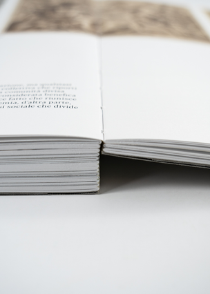 A thick open book showing its exposed spine binding with sewn signatures and Italian body text visible on the pages. Sprint24 prints exposed spine thread-bound books without a cover — an artisanal binding technique that highlights the stitching and gives fine editions a unique, handcrafted character.