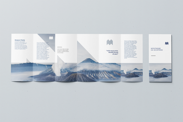 A fully open six-panel brochure with a minimalist white layout featuring a dramatic blue-toned volcanic mountain panorama spanning the central panels, flanked by clean text columns and an 'M' monogram logo. Custom-printed six-panel brochures with full-width landscape photography create a visually striking canvas ideal for travel brands, hospitality groups and destination marketing campaigns.