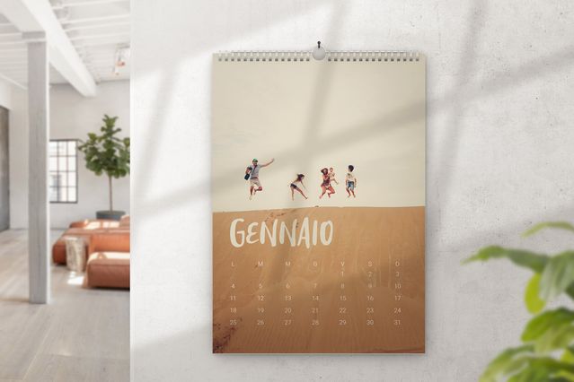 A spiral-bound wall photo calendar hanging on a bright white wall showing the January page with a warm sepia desert scene featuring a family silhouette walking and the month name in handwritten style lettering. Custom photo wall calendars are the perfect personalised gift for friends and family — available with your own photos, printed on photo paper and orderable from just one copy.