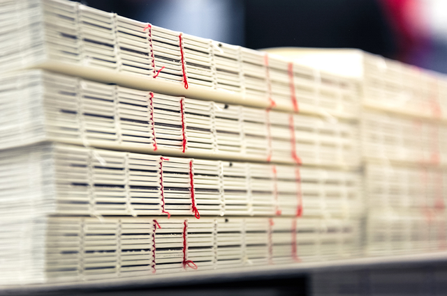 Multiple stacks of book blocks with red exposed thread binding visible along the spines, photographed in a print production environment. Sprint24 specialises in exposed spine thread binding for fine editions, catalogues and unique publications — a distinctive artisanal technique that turns the binding itself into a design element.
