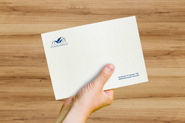 A premium Tintoretto Neve envelope with hammered snow-effect paper, branded logo and printed return address held in a hand over a warm wooden desk. Sprint24 prints Tintoretto Neve envelopes on FSC-certified pure cellulose paper with hammered texture — ideal for wedding invitations, prestige events and refined corporate communication with optional hot foil stamping.