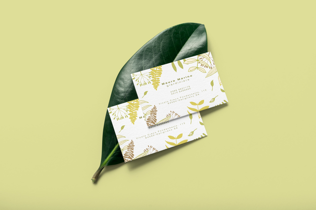 Two custom white business cards with a yellow-green botanical leaf pattern for 'Maria Mattera' displayed on a large tropical leaf against a lime green background. Custom-printed gardener business cards with nature-inspired botanical designs help landscape professionals and garden service providers communicate their brand identity and attract new clients.