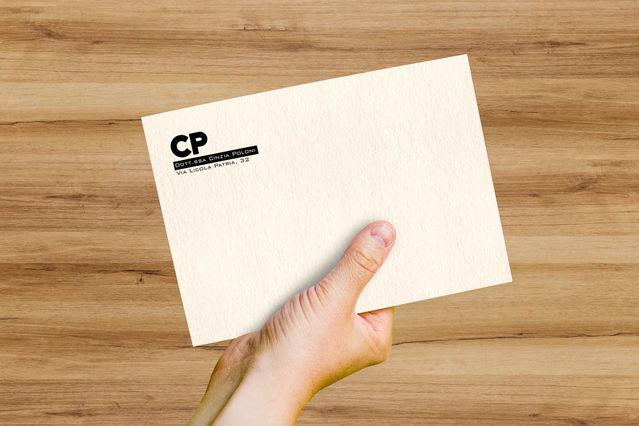 A Freelife Vellum White envelope with slightly antiqued parchment-style paper, branded 'CP' logo and printed return address held over a wooden surface. Sprint24 prints Vellum White envelopes on FSC-certified recycled paper made of pure cellulose and cotton — ideal for eco-conscious brands, refined invitations and corporate stationery with a velvety touch.