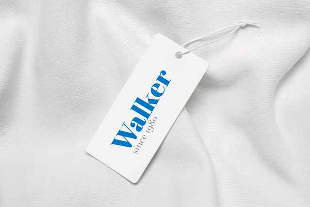 A shaped white clothing hang tag for the Walker brand resting on white fabric, featuring elegant blue serif typography. The clean minimalist design highlights the brand name prominently. An excellent example of custom shaped clothing tags for premium fashion labels.
