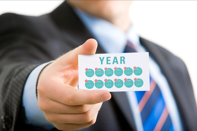 A compact pocket calendar card displayed in a business professional's hand, showcasing the portable design perfect for wallets and daily carry. Featuring a clean white layout with blue date tracking elements, this laminated pocket calendar combines functionality with professional appearance. Sprint24's online printing service lets you customize pocket calendars in bulk for corporate gifts or pers…