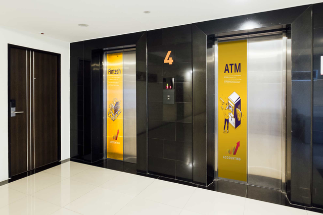 Large-format adhesive PVC applied to flat black walls featuring bright yellow wayfinding graphics including ATM, floor numbers, and directional icons for modern commercial spaces. Showcases professional installation with clean edges, bubble-free application, and excellent durability in high-traffic interior environments. Perfect for office buildings, commercial facilities, and institutional space…